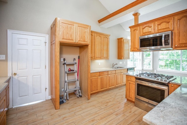 kitchen featuring sink, vaulted ceiling, light stone countertops, appliances with stainless steel finishes, and light hardwood / wood-style floors