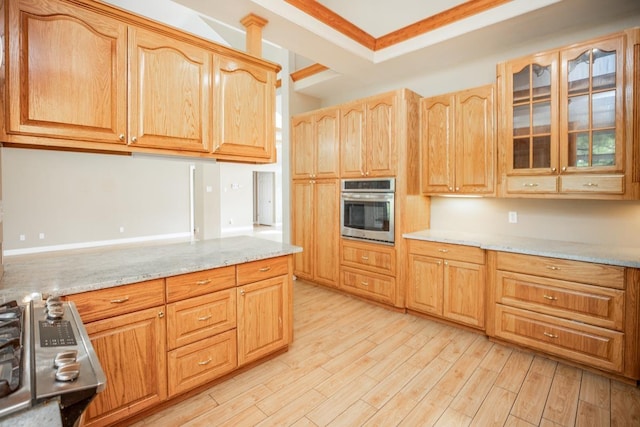 kitchen with stainless steel oven, light stone counters, ornamental molding, and light hardwood / wood-style flooring