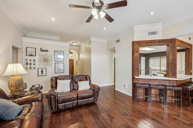 living room with wood finished floors, ceiling fan, baseboards, ornamental molding, and visible vents