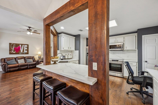 kitchen with a ceiling fan, a breakfast bar area, white cabinetry, backsplash, and appliances with stainless steel finishes