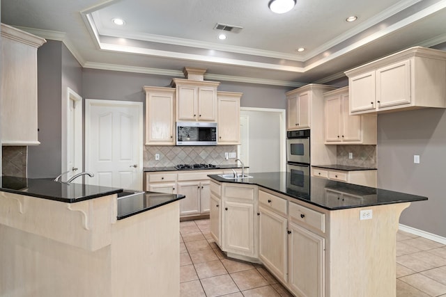 kitchen with stainless steel appliances, an island with sink, a breakfast bar area, and a tray ceiling