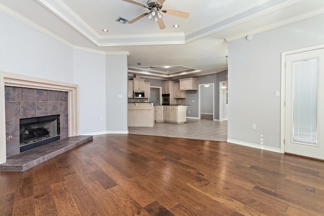 unfurnished living room featuring a raised ceiling, crown molding, hardwood / wood-style flooring, and ceiling fan