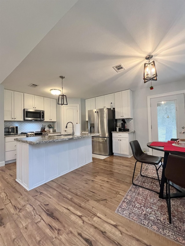 kitchen featuring stainless steel appliances, an island with sink, white cabinets, and light hardwood / wood-style floors