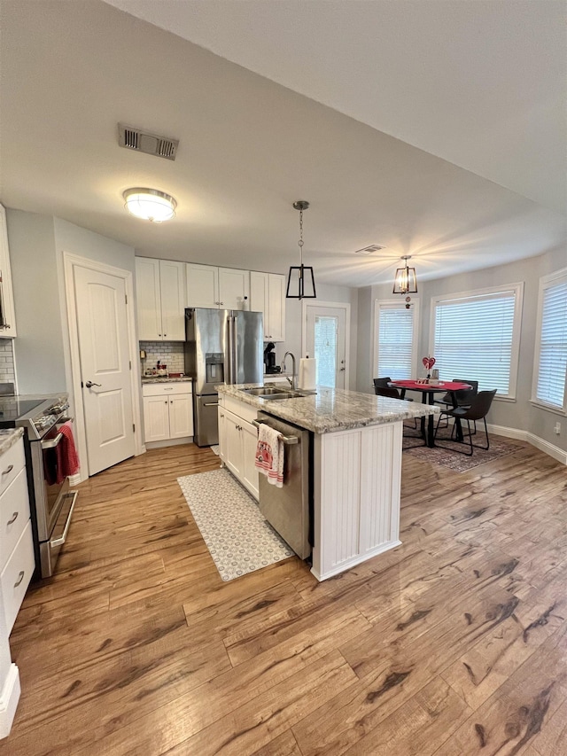 kitchen featuring sink, appliances with stainless steel finishes, white cabinetry, hanging light fixtures, and a center island with sink