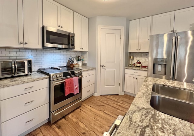 kitchen featuring sink, backsplash, stainless steel appliances, light hardwood / wood-style floors, and white cabinets