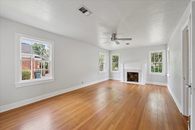 623 20th St, Beaumont, TX 77706 - unfurnished living room featuring ceiling fan, healthy amount of natural light, light wood-style floors, baseboards, and a textured ceiling