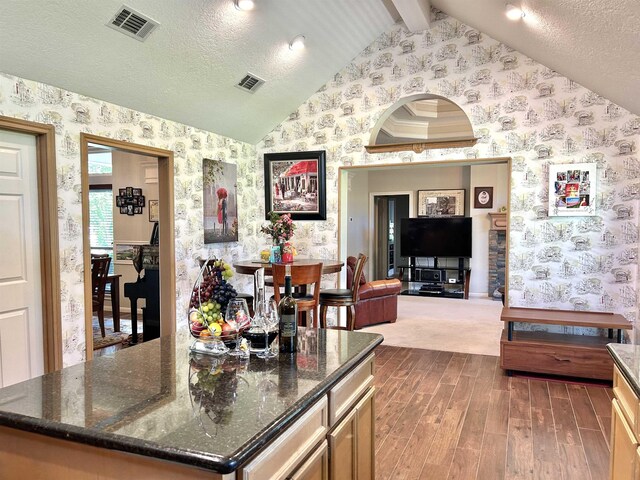 kitchen with vaulted ceiling with beams, a textured ceiling, a kitchen island, and dark stone countertops