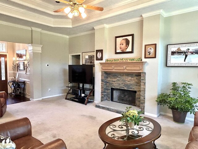 living room featuring carpet, a raised ceiling, a stone fireplace, crown molding, and ceiling fan