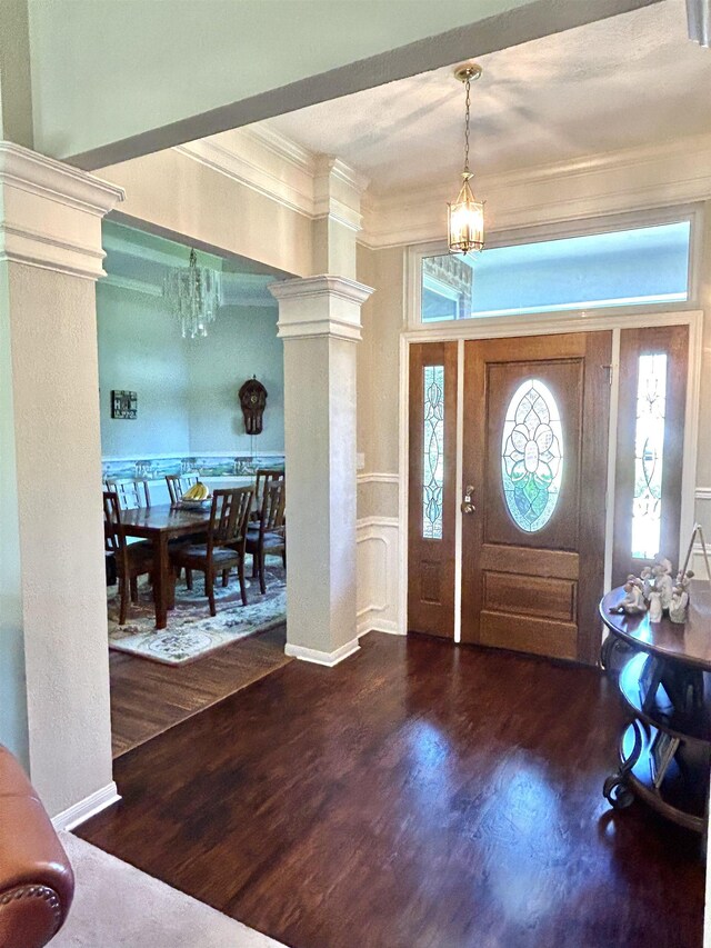 entrance foyer with hardwood / wood-style floors, ornate columns, crown molding, and a chandelier