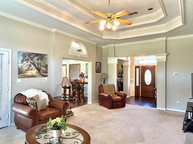 carpeted living room with ornate columns, ceiling fan, a high ceiling, a raised ceiling, and crown molding