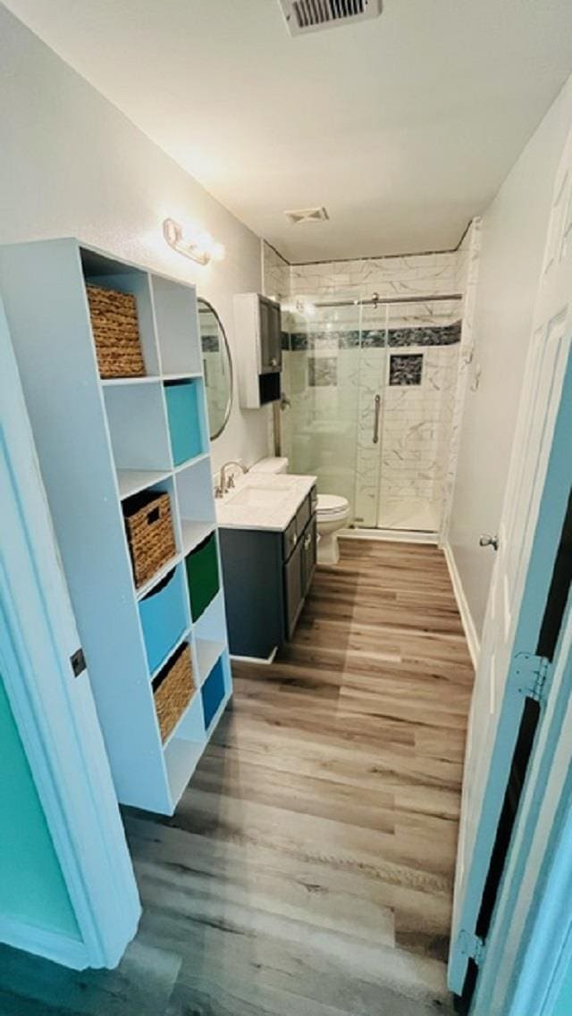 bathroom featuring wood-type flooring, a shower with shower door, vanity, and toilet