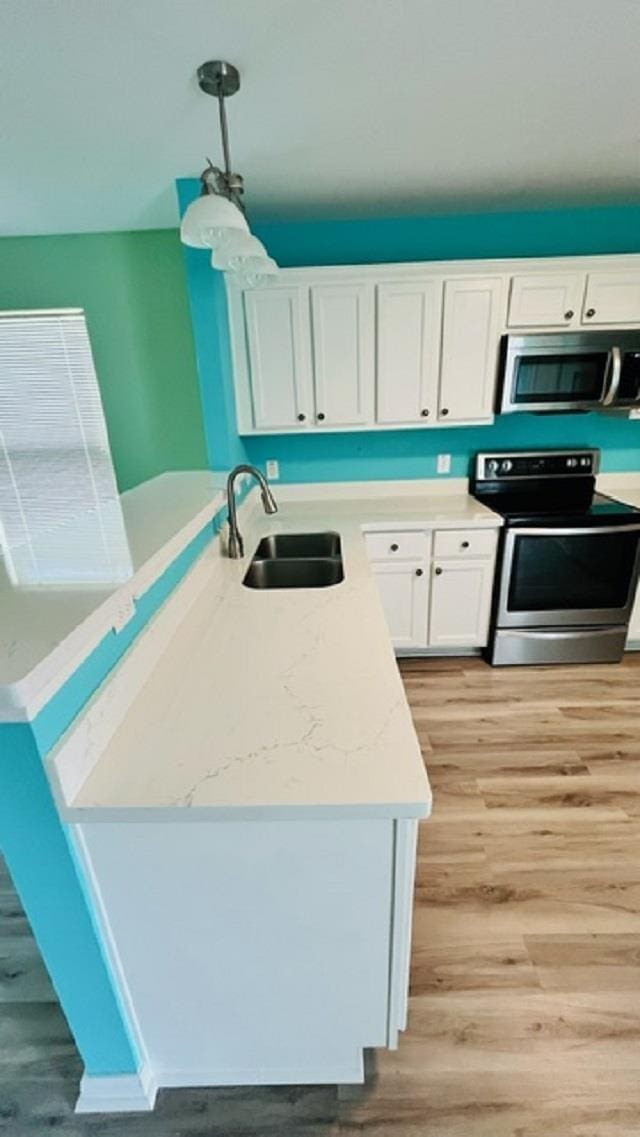 kitchen with sink, light hardwood / wood-style flooring, appliances with stainless steel finishes, hanging light fixtures, and white cabinets