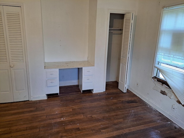 unfurnished bedroom with dark hardwood / wood-style flooring, built in desk, and multiple closets