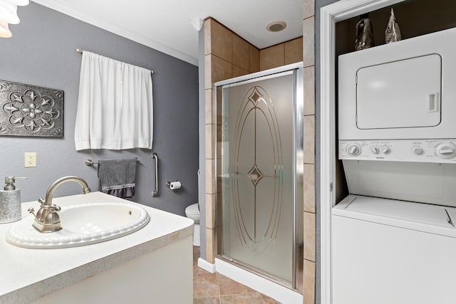 bathroom featuring vanity, stacked washing maching and dryer, an enclosed shower, and toilet