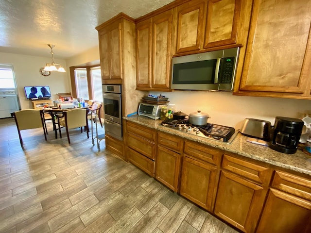 kitchen featuring decorative light fixtures, light stone counters, stainless steel appliances, and an inviting chandelier