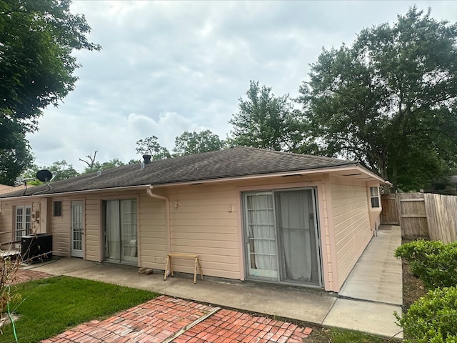 rear view of property featuring a patio, roof with shingles, and fence
