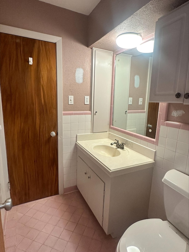 bathroom featuring tile patterned flooring, vanity, toilet, tile walls, and a wainscoted wall
