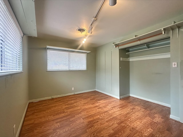 unfurnished bedroom featuring track lighting, visible vents, multiple windows, and wood finished floors