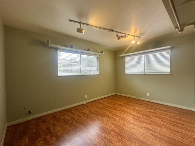 empty room featuring baseboards, rail lighting, and wood finished floors