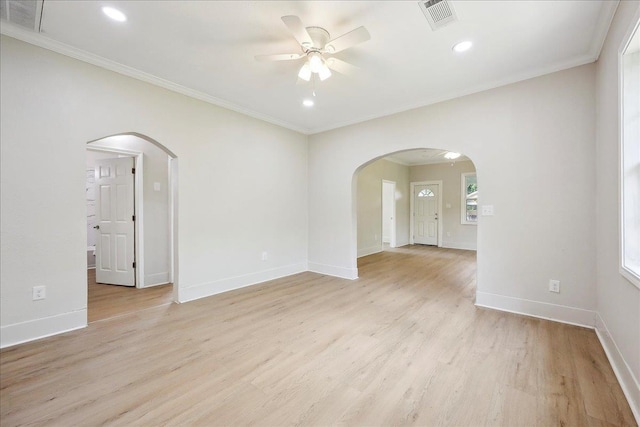 empty room featuring crown molding, ceiling fan, visible vents, arched walkways, and light wood-type flooring