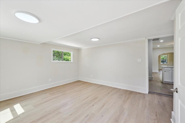 unfurnished room featuring light wood-style flooring, arched walkways, baseboards, recessed lighting, and ornamental molding
