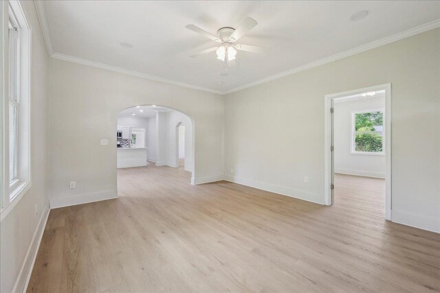 empty room with crown molding, light wood finished floors, arched walkways, and a ceiling fan