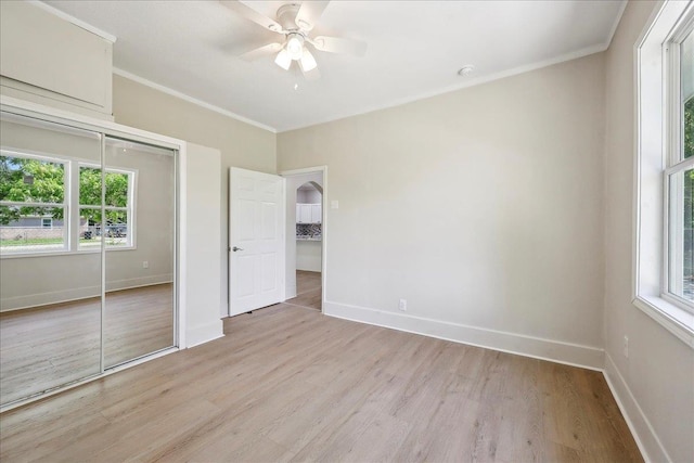 unfurnished bedroom featuring ornamental molding, a closet, multiple windows, and light wood-type flooring