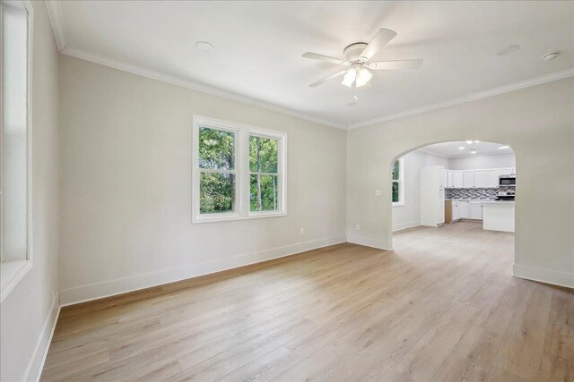 spare room featuring arched walkways, ornamental molding, and light wood-style flooring