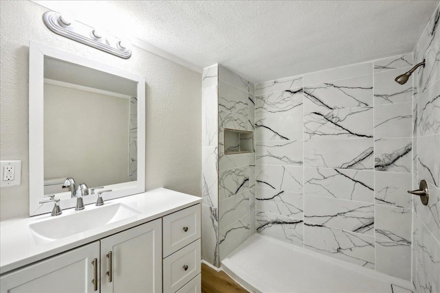 full bathroom featuring a tile shower, a textured ceiling, a textured wall, and vanity