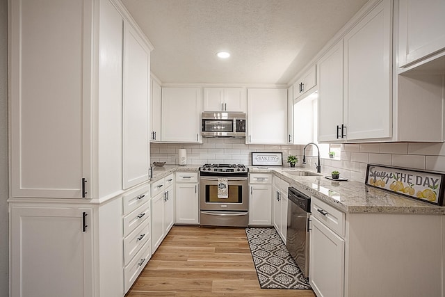 kitchen with white cabinetry, sink, light stone counters, appliances with stainless steel finishes, and light wood-type flooring