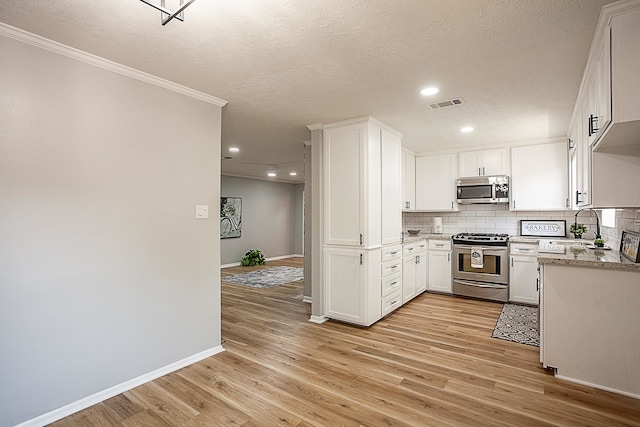 kitchen with white cabinets, sink, appliances with stainless steel finishes, tasteful backsplash, and light hardwood / wood-style floors