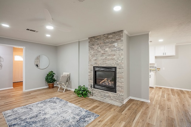 living area with light hardwood / wood-style flooring, ceiling fan, a stone fireplace, and crown molding