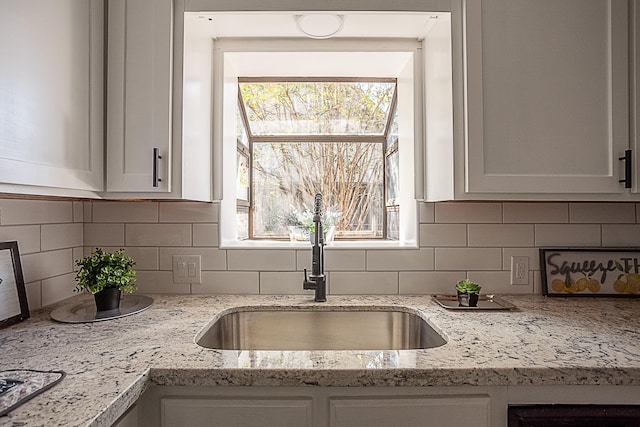 kitchen with light stone countertops, backsplash, white cabinetry, and sink