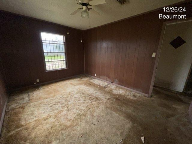 unfurnished room with ceiling fan, carpet floors, and wood walls