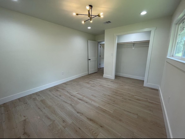 unfurnished bedroom with light hardwood / wood-style floors, an inviting chandelier, and a closet