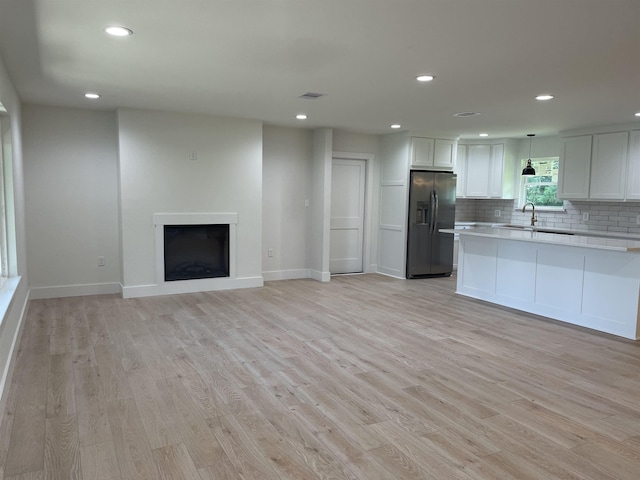 kitchen with hanging light fixtures, light hardwood / wood-style flooring, stainless steel refrigerator with ice dispenser, decorative backsplash, and white cabinets