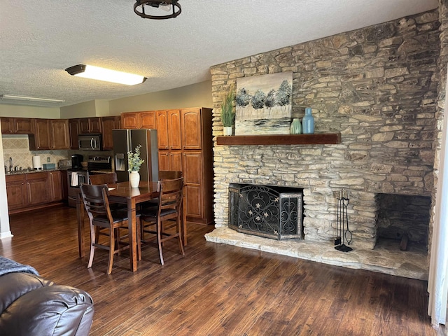 dining space with a stone fireplace, sink, dark wood-type flooring, and a textured ceiling