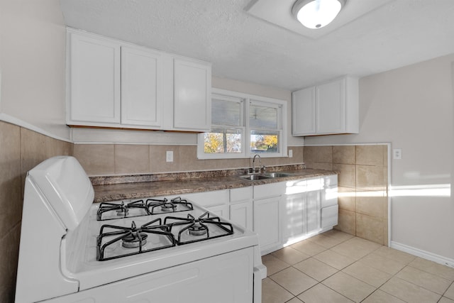 kitchen with sink, white gas range, a textured ceiling, light tile patterned floors, and white cabinetry