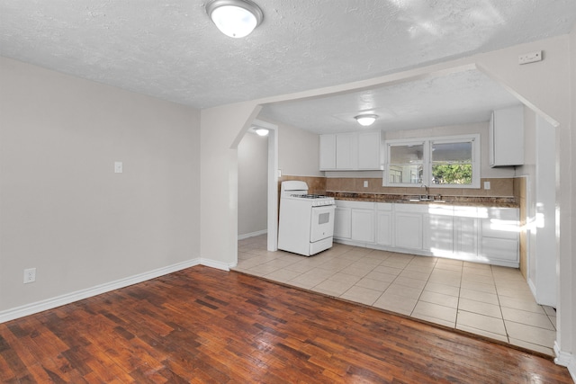 kitchen featuring white gas range oven, backsplash, sink, light hardwood / wood-style floors, and white cabinetry