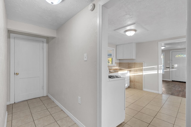 hall with light tile patterned floors, a textured ceiling, and washer / dryer