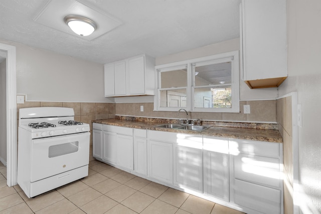 kitchen with decorative backsplash, white range with gas cooktop, sink, white cabinetry, and light tile patterned flooring