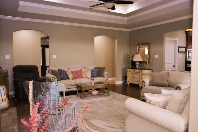 living area with arched walkways, ceiling fan, and a tray ceiling