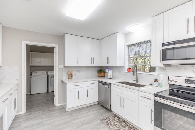 kitchen with white cabinetry, light countertops, washer and clothes dryer, stainless steel appliances, and a sink