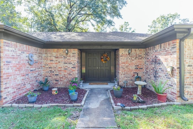 doorway to property featuring brick siding and a shingled roof