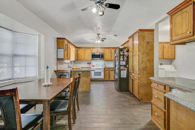 kitchen featuring dark wood-type flooring, vaulted ceiling, ceiling fan, independent washer and dryer, and appliances with stainless steel finishes