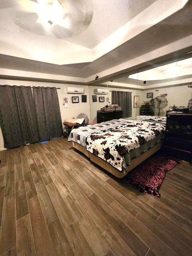 bedroom featuring ceiling fan, a wall mounted air conditioner, a raised ceiling, a textured ceiling, and hardwood / wood-style flooring