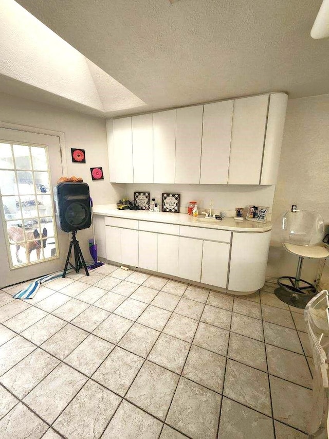 kitchen with a textured ceiling, white cabinetry, and sink