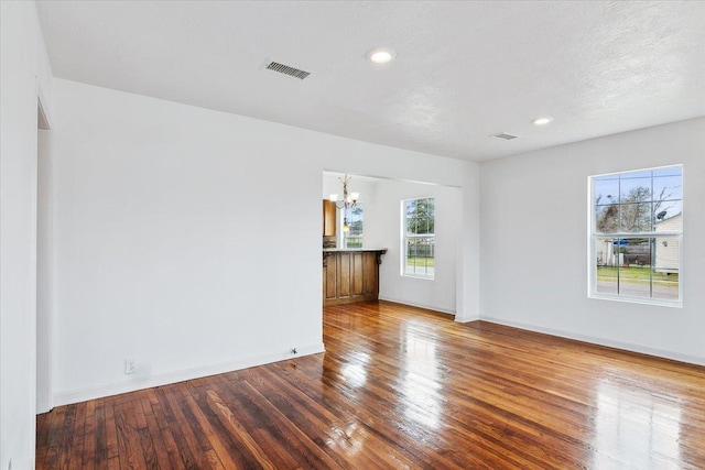 empty room featuring a textured ceiling, an inviting chandelier, and hardwood / wood-style floors