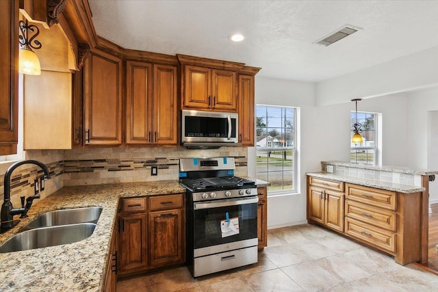 kitchen featuring appliances with stainless steel finishes, sink, backsplash, hanging light fixtures, and light stone counters