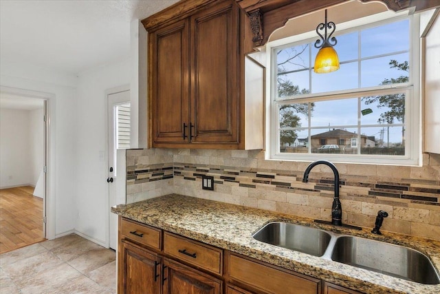 kitchen with light stone counters, sink, backsplash, and pendant lighting